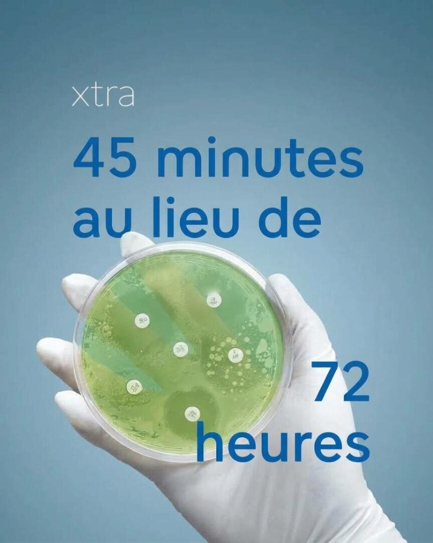 Une main gantée tient une boîte de Pétri contenant une culture bactérienne, avec la mention xtra 45 minutes au lieu de 72 heures.