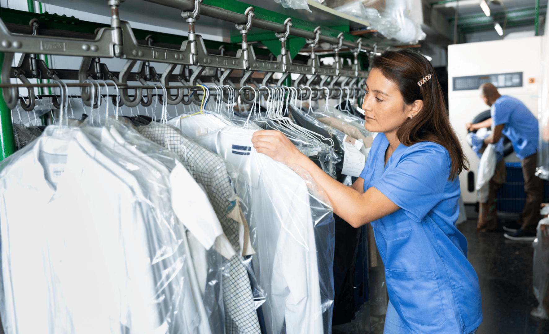 Une femme en uniforme bleu trie des vêtements nettoyés à sec sur un tapis roulant dans une blanchisserie.
