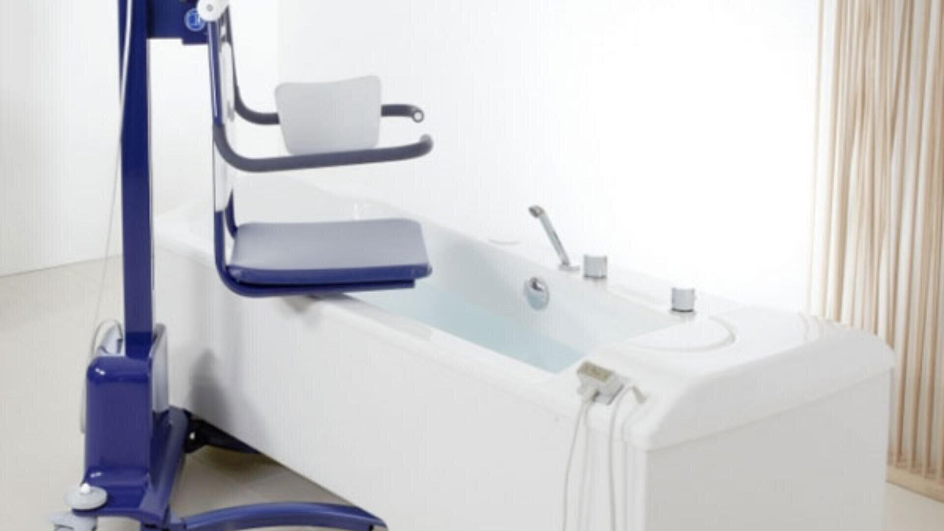 Ein blau-weißer Badelift-Stuhl, der neben einer Pflegebadewanne in einem minimalistisch gestalteten, hellen Badezimmer steht. Der Stuhl soll den Benutzern helfen, sicher in die Badewanne ein- und auszusteigen.