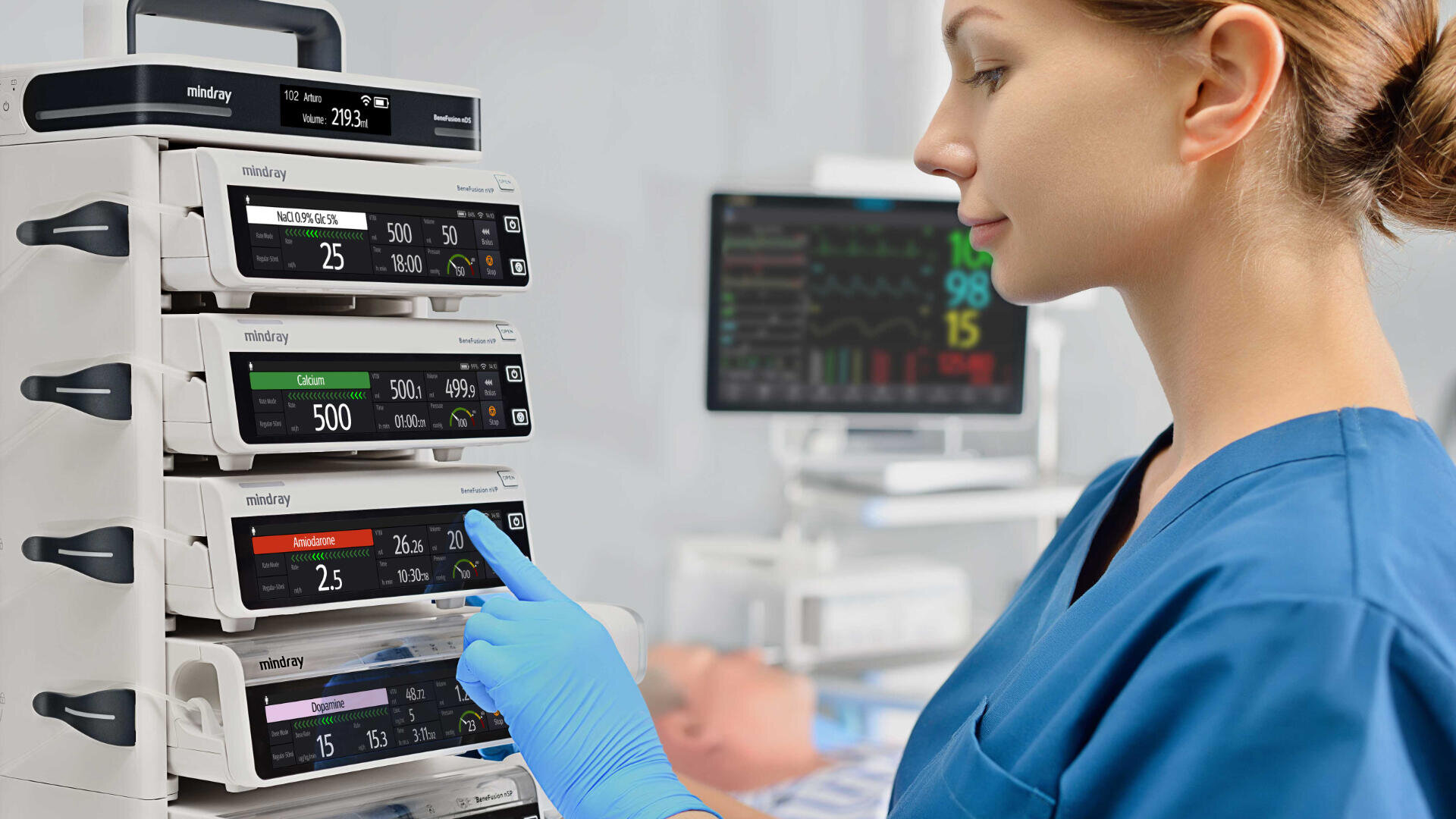 Ein Mitarbeiter des Gesundheitswesens in blauem Kittel und Handschuhen stellt in einem Krankenhauszimmer eine medizinische Infusionspumpe ein, während im Hintergrund ein Patientenmonitor und eine unscharfe Schaufensterpuppe zu sehen sind.