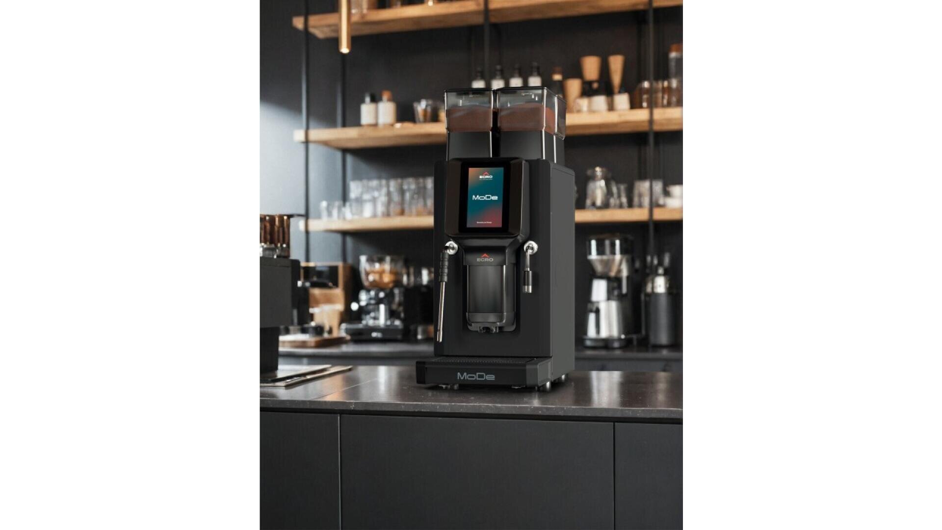 Une machine à café automatique moderne est posée sur un comptoir de cuisine sombre, avec des étagères de tasses, de bocaux et de matériel de café en arrière-plan. La machine est dotée d'un écran tactile numérique et de deux trémies à grains sur le dessus.