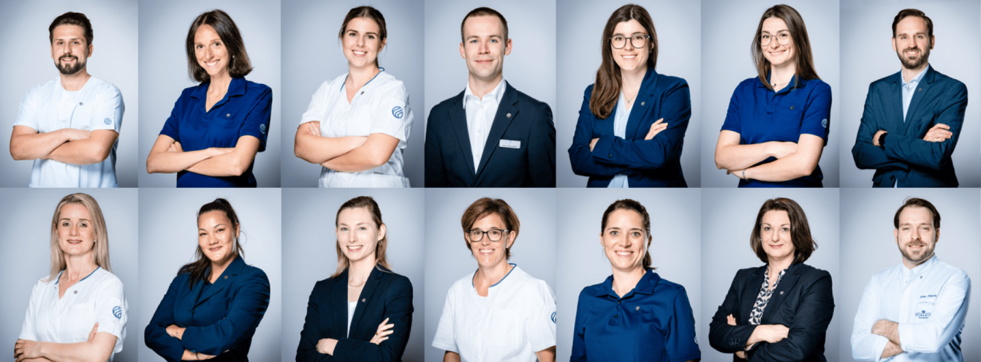 Ein Gruppenporträt von fünfzehn Berufstätigen, Männern und Frauen, die in zwei Reihen stehen und in die Kamera lächeln. Die meisten von ihnen tragen Uniformen oder Geschäftskleidung und haben die Arme vor einem hellgrauen Hintergrund verschränkt.