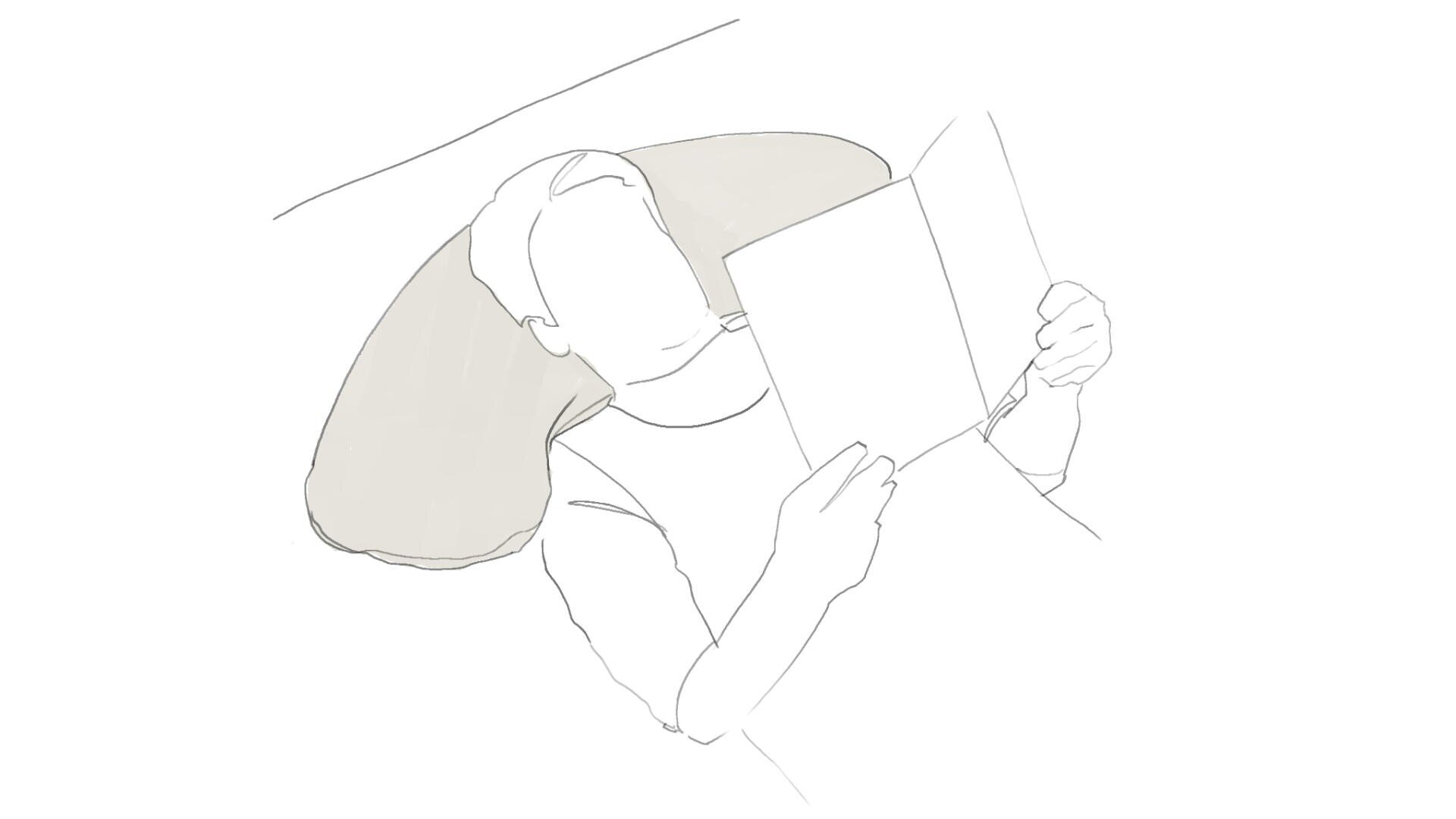 Eine Person, die mit einem U-förmigen Kissen hinter dem Kopf liegt und ein aufgeschlagenes Buch hält und liest.