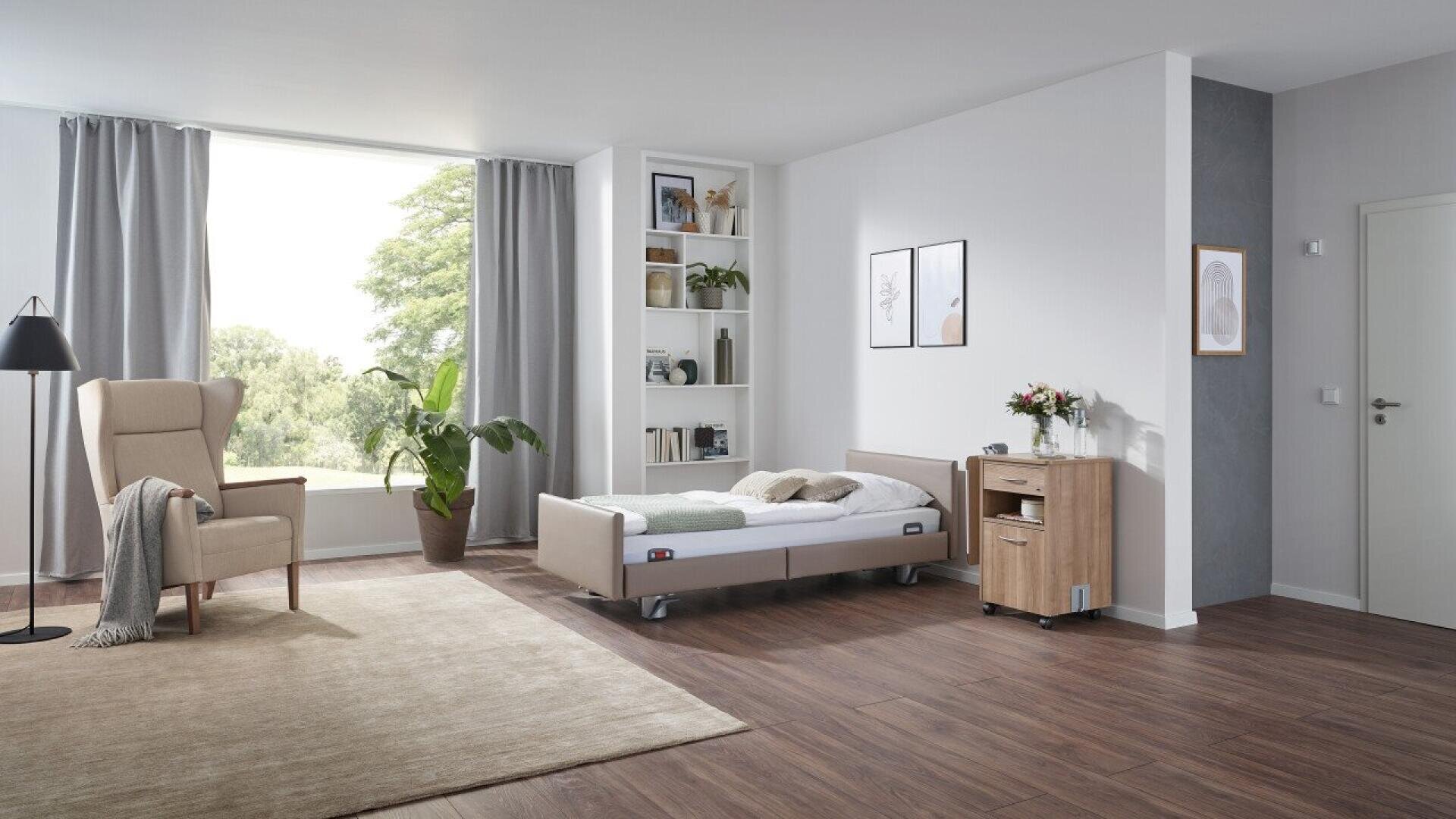 Une chambre à coucher moderne et confortable avec un lit de type hospitalier, un fauteuil, du parquet, des étagères décorées, des plantes en pot, une grande fenêtre avec des rideaux gris et une table de chevet avec des fleurs et des livres.