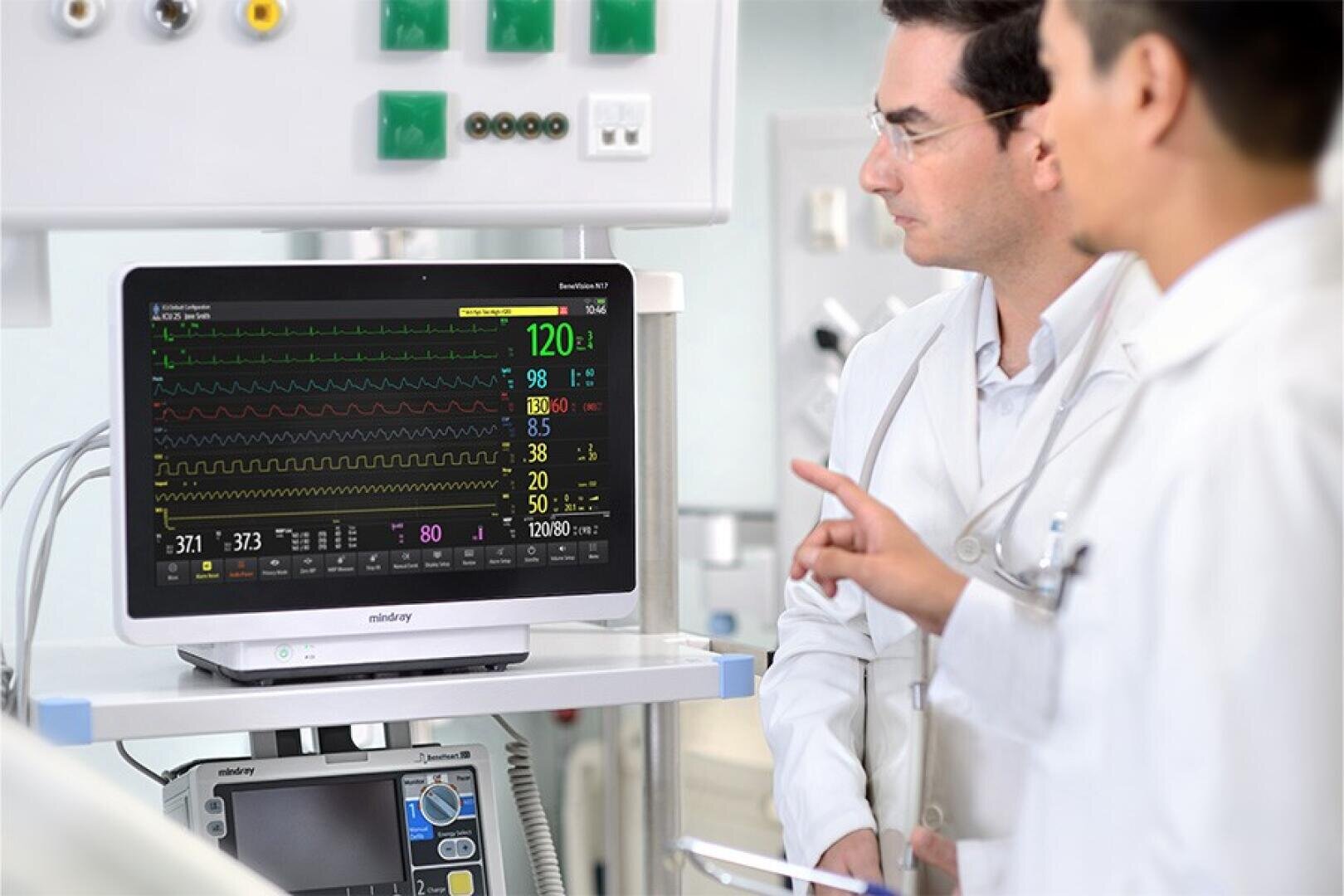 Zwei Ärzte in weißen Kitteln blicken auf einen Überwachungsbildschirm, auf dem die Vitalwerte eines Patienten angezeigt werden.