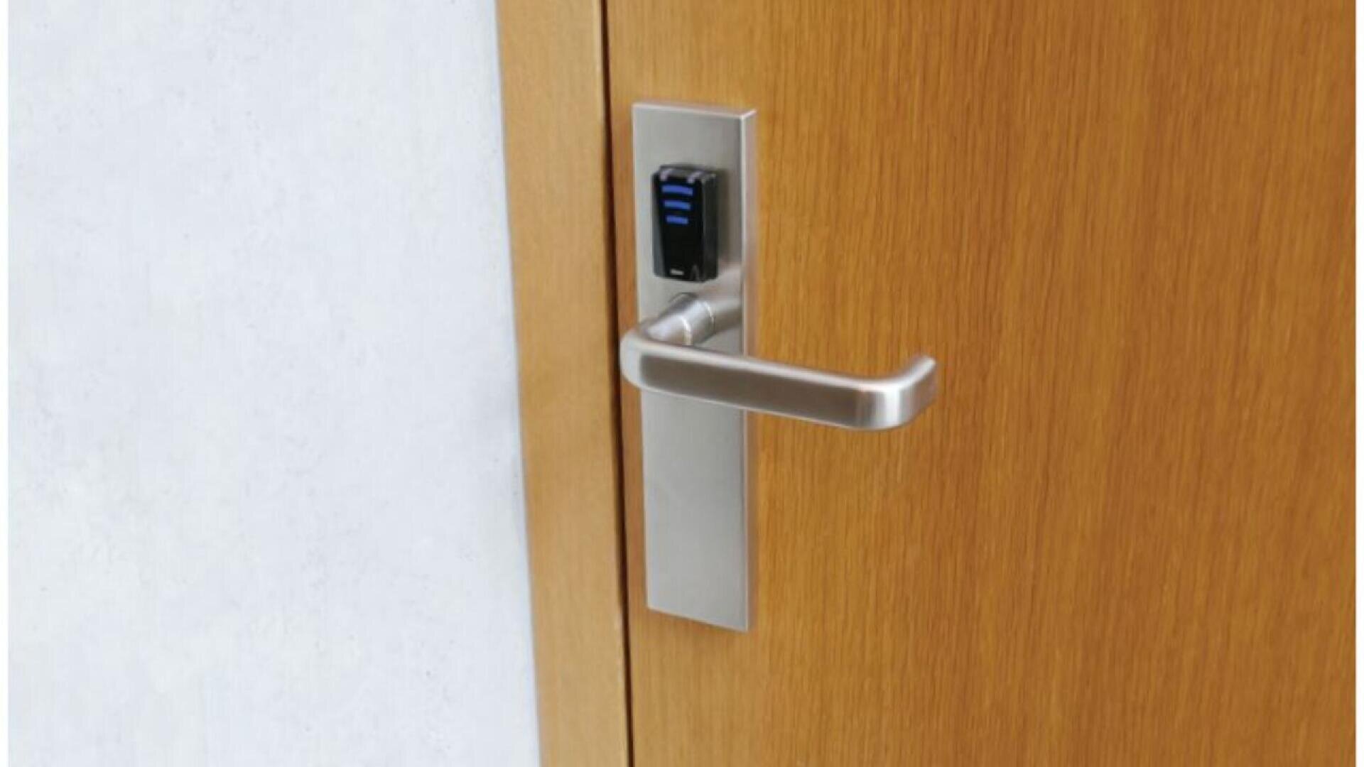 Gros plan sur une porte en bois dotée d'une poignée moderne en argent et d'une serrure à lecteur de carte électronique montée au-dessus de la poignée. La porte est placée contre un mur blanc.