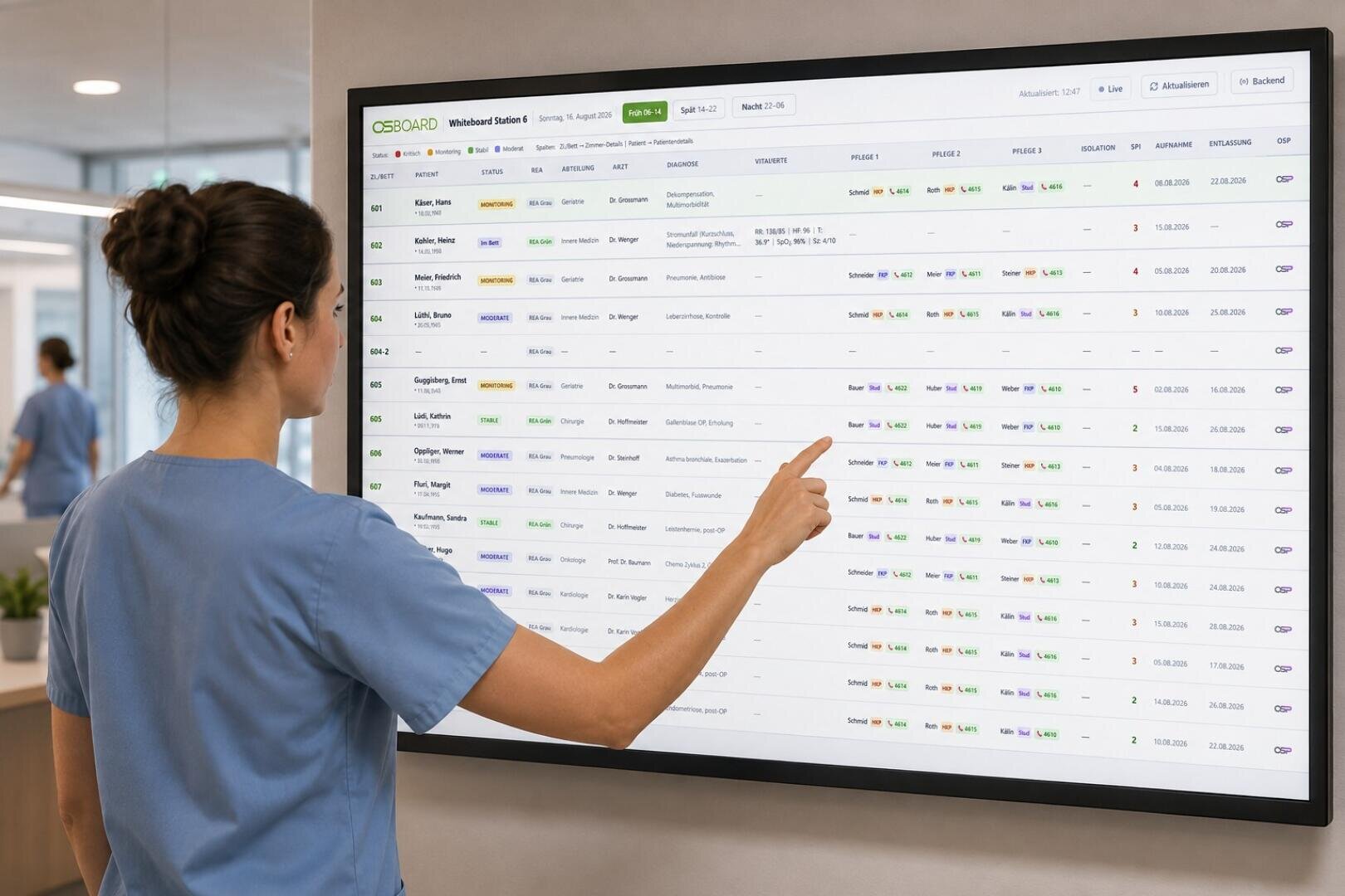 Dans un établissement médical, une femme vêtue d'une blouse bleue touche un grand écran tactile fixé au mur, sur lequel s'affichent la liste des noms des patients, leur état et leurs horaires.
