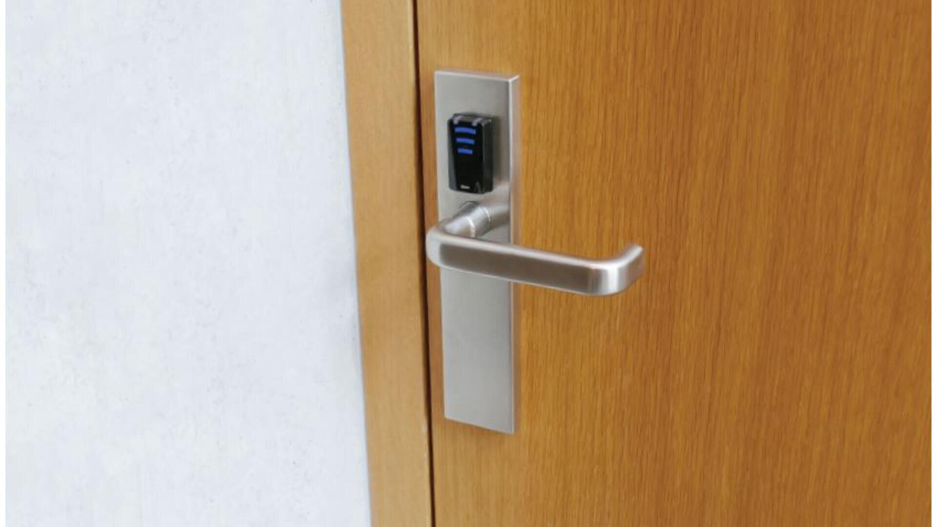 Abgebildet ist eine Holztür mit einem modernen silbernen Griff und einem elektronischen Schloss mit einem kleinen schwarzen Tastenfeld mit blauen Kontrollleuchten. Die Tür ist teilweise in eine weiße Wand eingelassen.