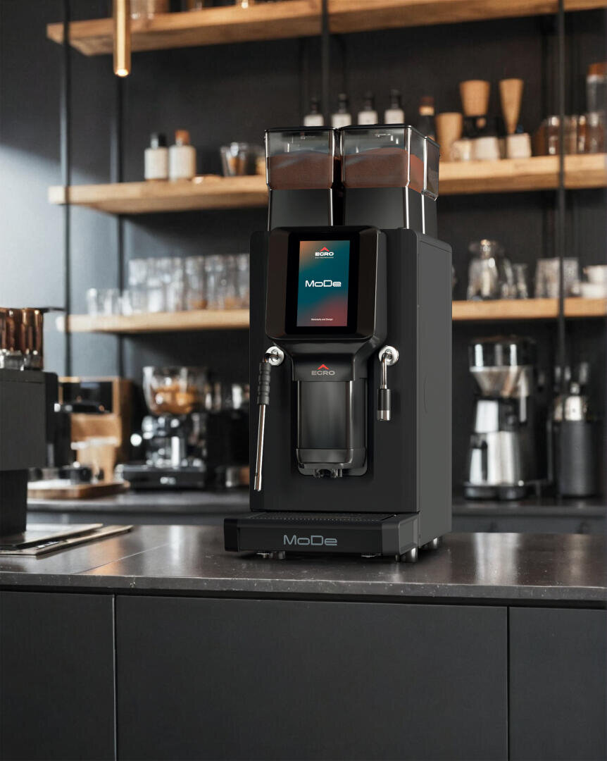 Eine moderne schwarze Kaffeemaschine mit digitaler Anzeige steht auf einer dunklen Arbeitsplatte in einem stilvollen Café. Im Hintergrund befinden sich Regale mit Tassen, Gläsern und Kaffeezubehör.