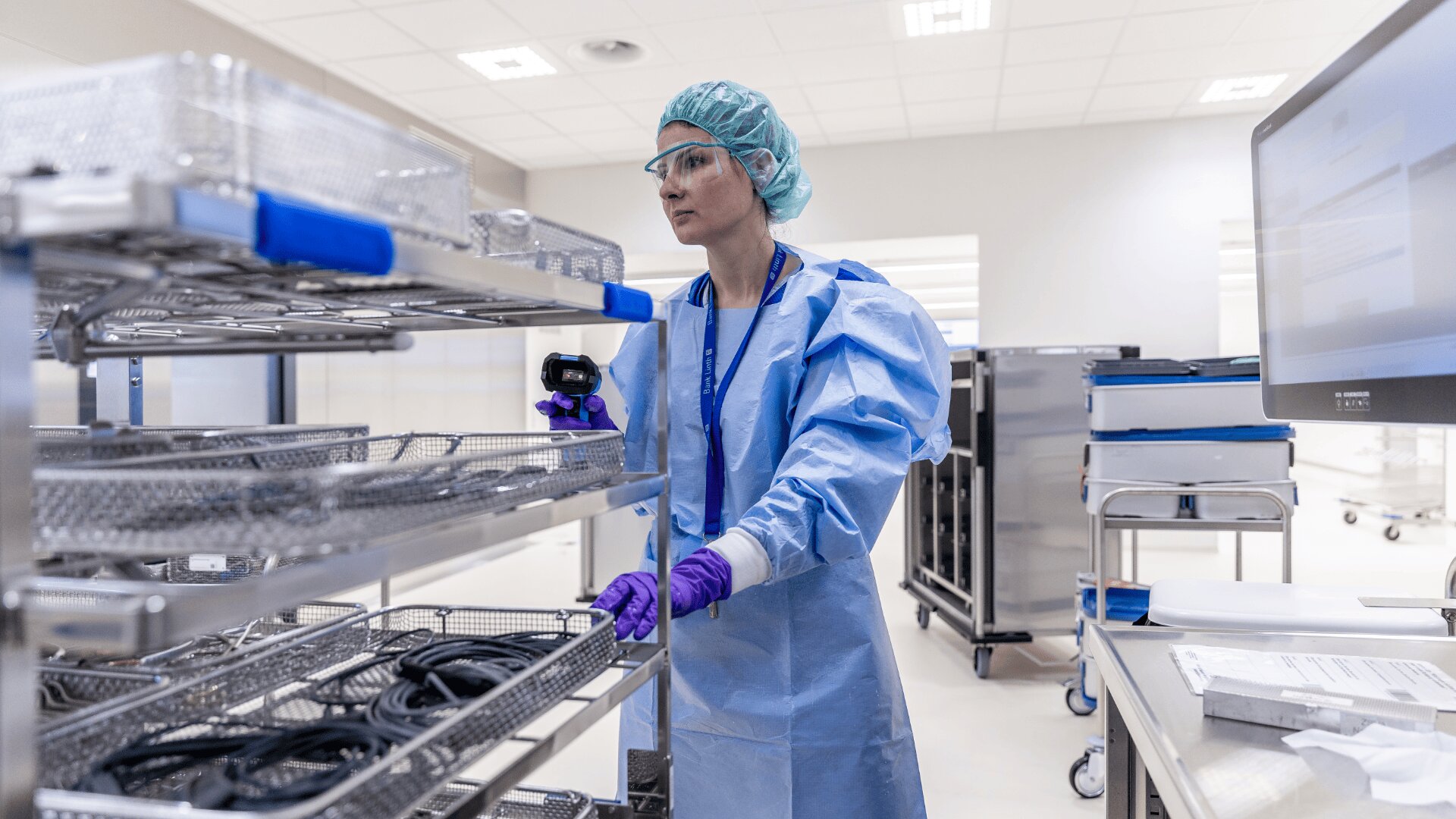 Ein Mitarbeiter des Gesundheitswesens in Schutzkleidung und Handschuhen ordnet und überprüft in einer sauberen, sterilen Krankenhausumgebung die Tabletts mit medizinischen Geräten auf Metallregalen.