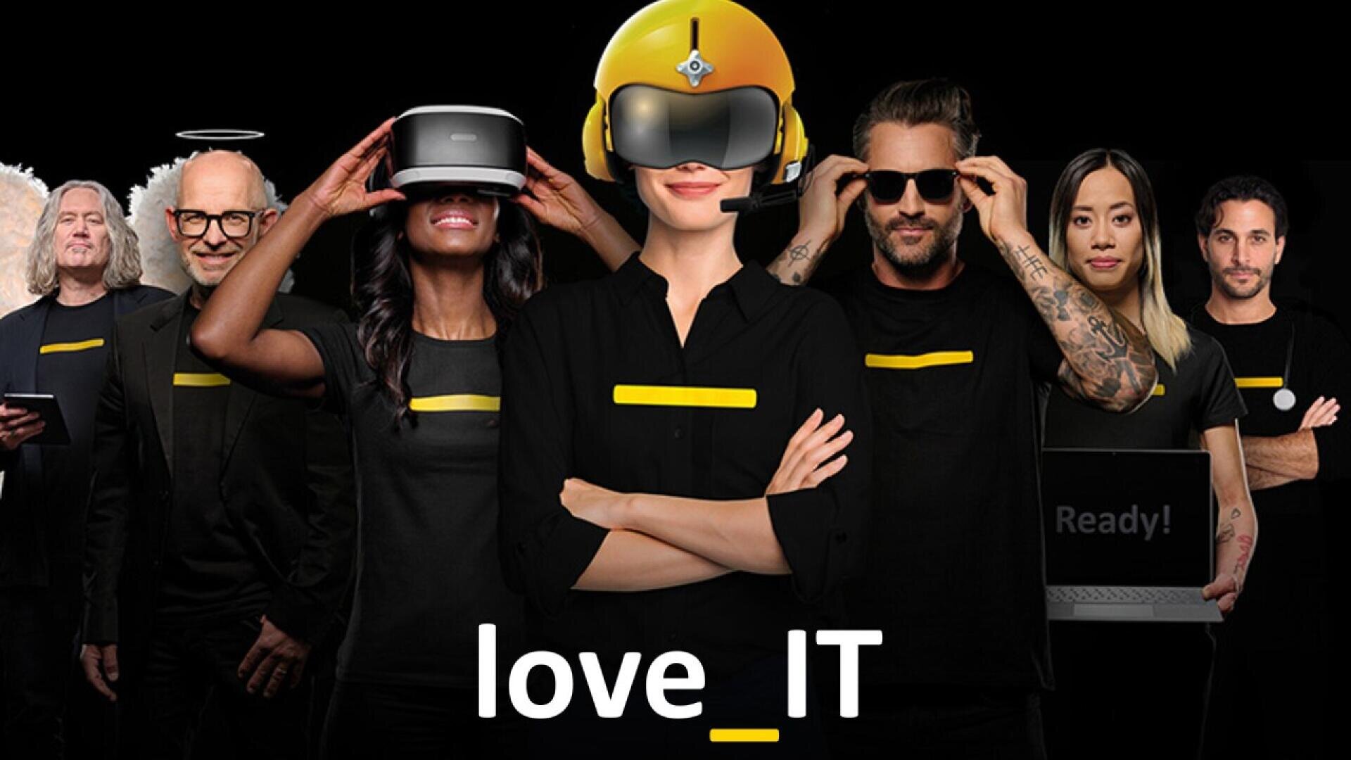 Un groupe diversifié de personnes portant des chemises noires avec des lignes jaunes se tient debout, confiant, certains utilisant des appareils technologiques tels que des casques VR et des ordinateurs portables. Le texte love_IT apparaît en dessous d'eux sur un fond noir.