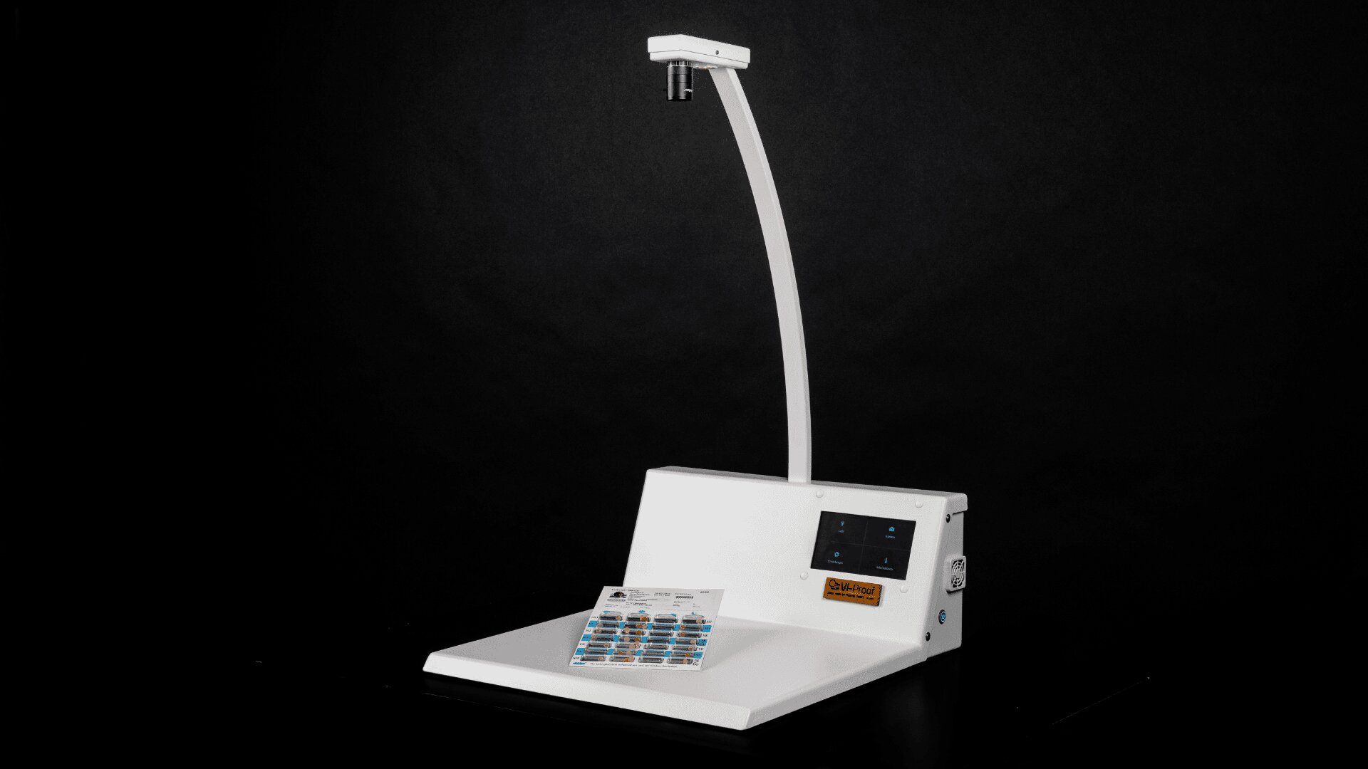 Ein weißes elektronisches Gerät mit einem Touchscreen, einem gebogenen Arm, der eine Kamera darüber hält, und einer Medikamentenablage auf seinem Sockel, alles vor einem schwarzen Hintergrund.