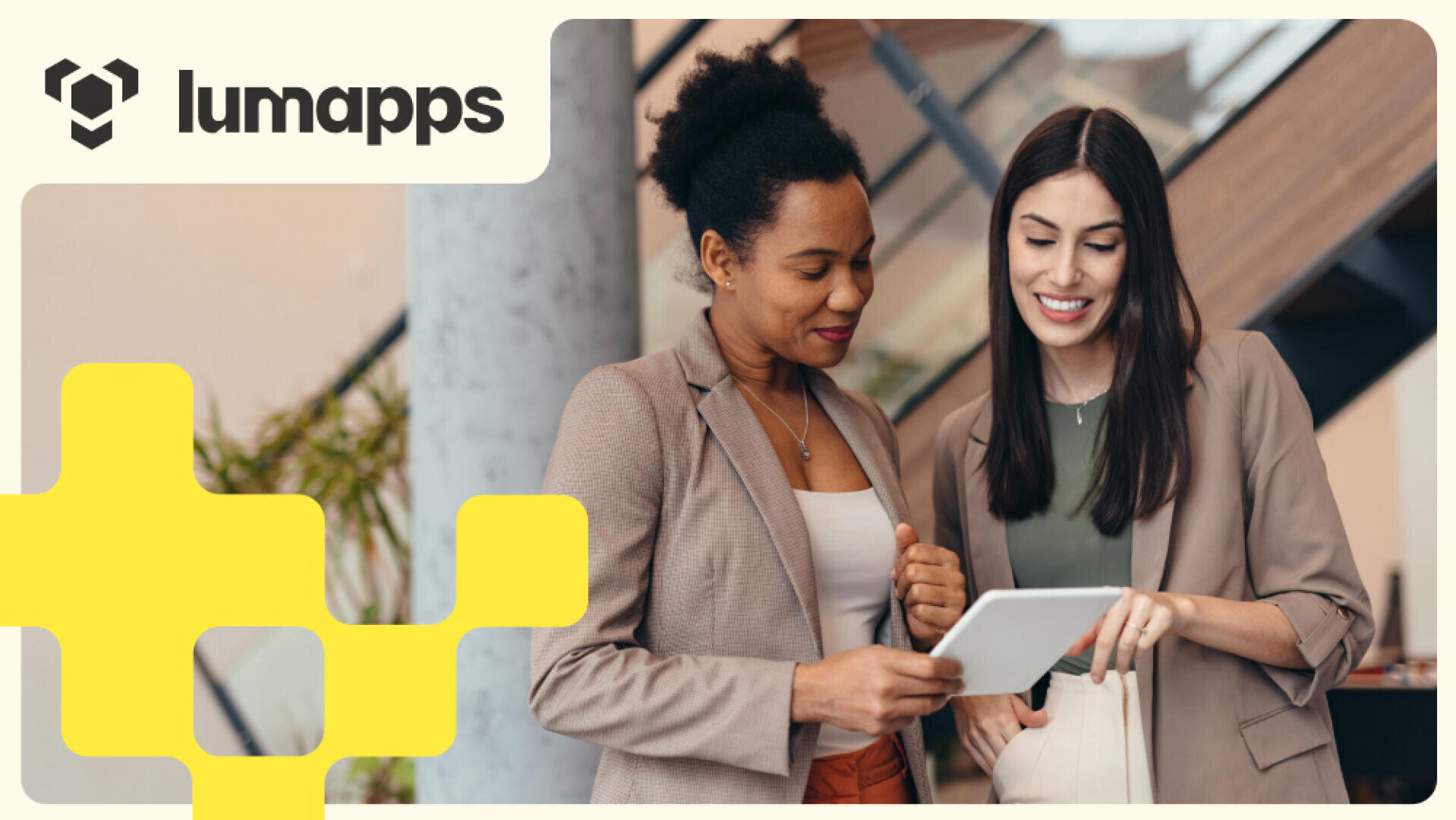 Zwei Frauen in Business-Kleidung lächeln und schauen gemeinsam auf ein Tablet. In der oberen linken Ecke ist das LumApps-Logo zu sehen, unten links befinden sich gelbe grafische Formen. Die Szene spielt in einem modernen Büro.