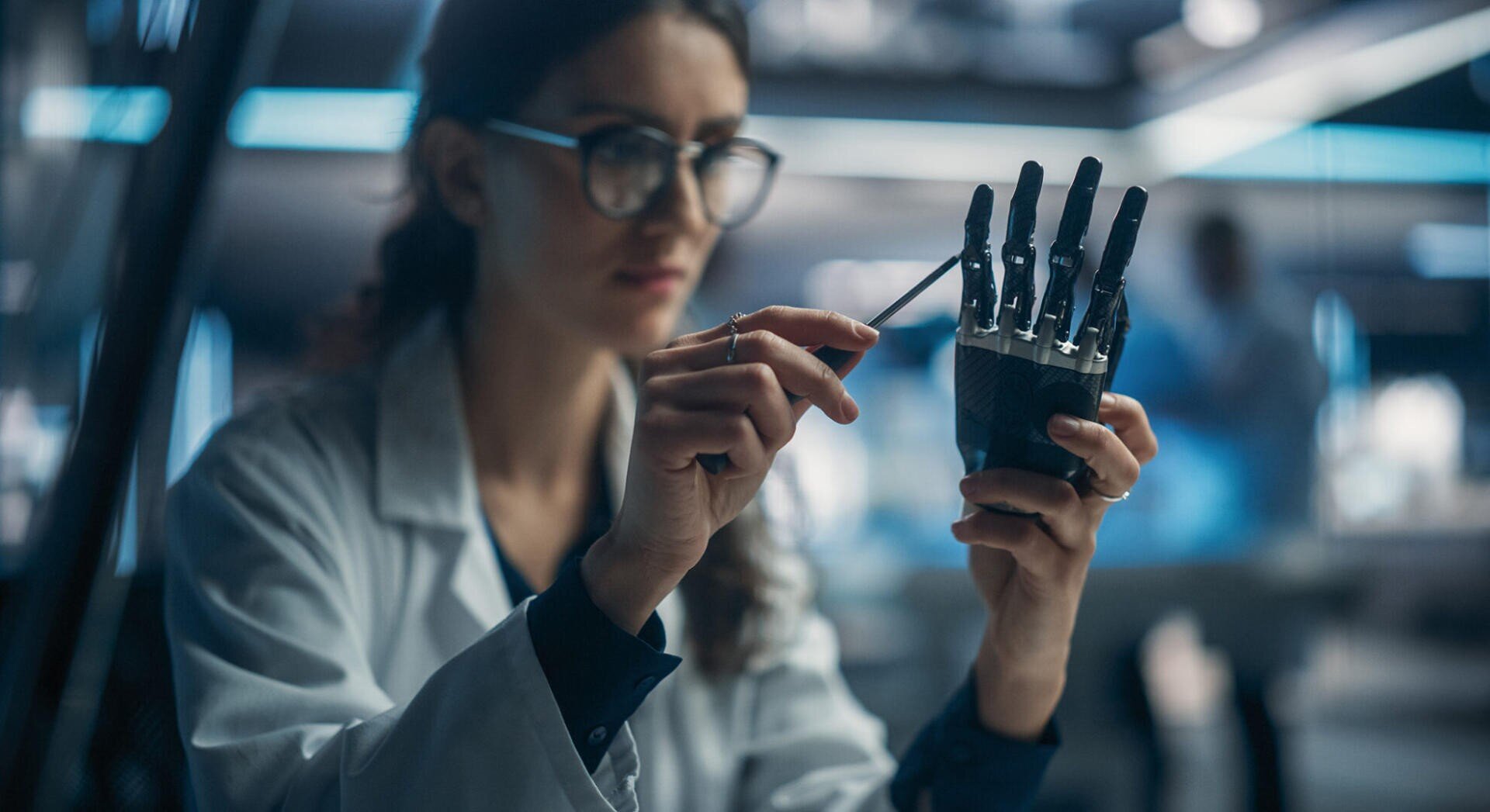 Une scientifique en blouse de laboratoire règle une main robotisée à l'aide d'un outil dans un laboratoire, tout en restant concentrée sur son travail.