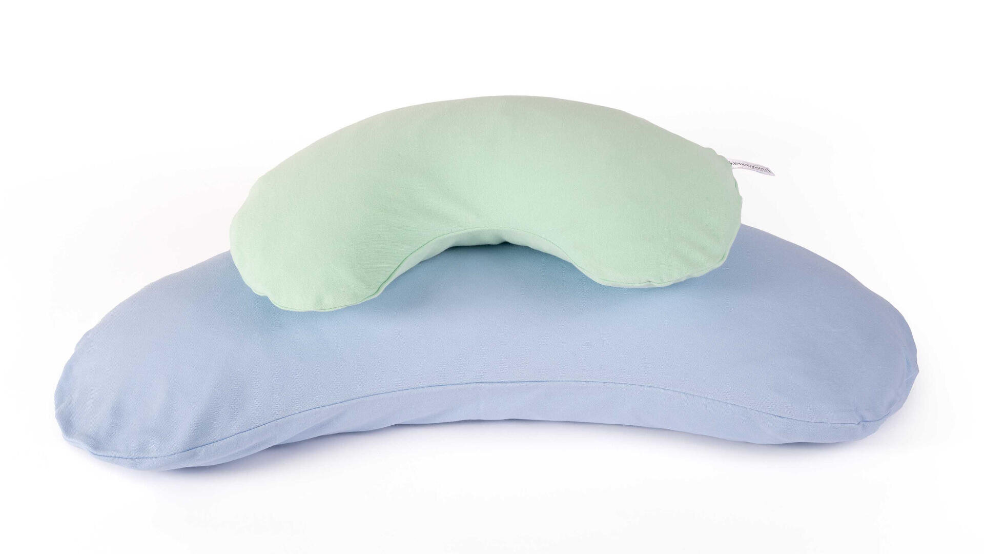 Zwei halbmondförmige Kissen, ein hellgrünes und ein kleineres, liegen auf einem größeren hellblauen Kissen, beide auf weißem Hintergrund.