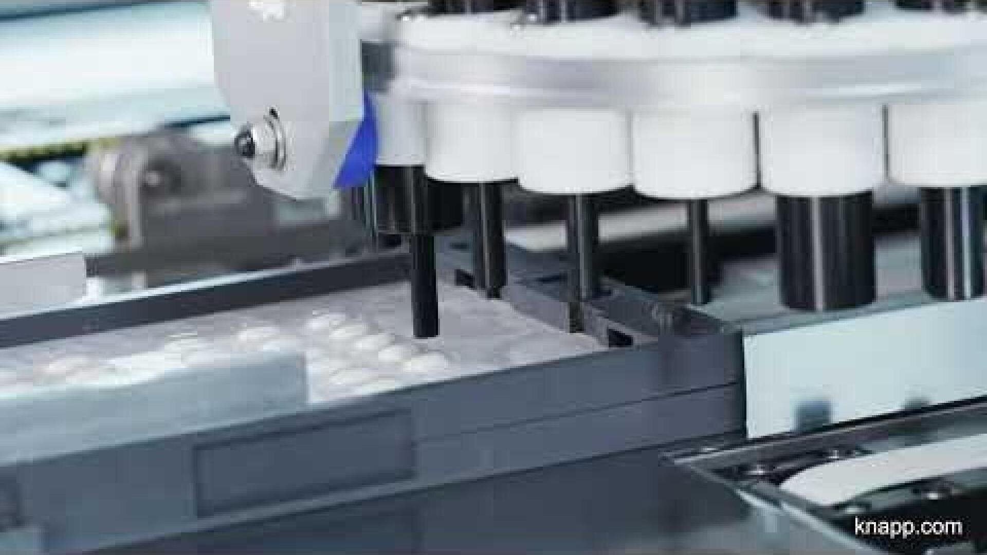 Nahaufnahme einer Maschine, die auf einer automatisierten pharmazeutischen Produktionslinie weiße Tabletten in eine Blisterverpackung einlegt.