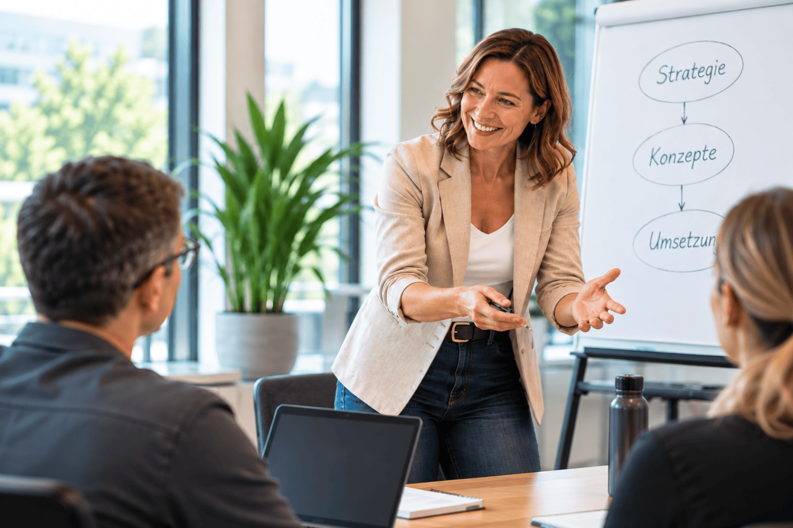 Une femme fait une présentation devant deux collègues et désigne un tableau blanc sur lequel figure un diagramme comportant les rubriques Stratégie, Concepts et Mise en œuvre.