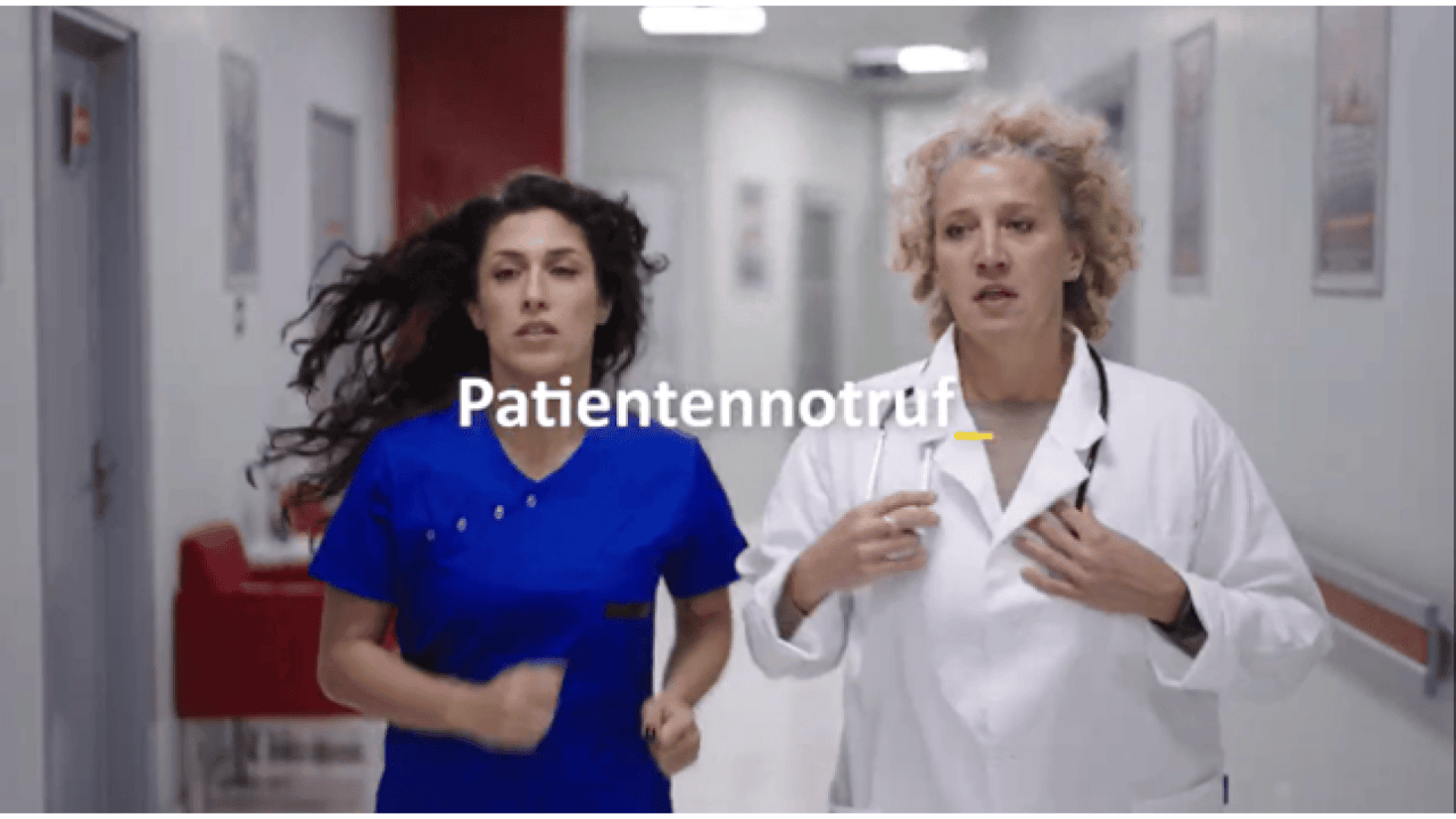 Zwei Mediziner, einer in blauem Kittel und einer in weißem Kittel, rennen eilig einen Krankenhausflur entlang. Das deutsche Wort "Patientennotruf" erscheint quer über das Bild.