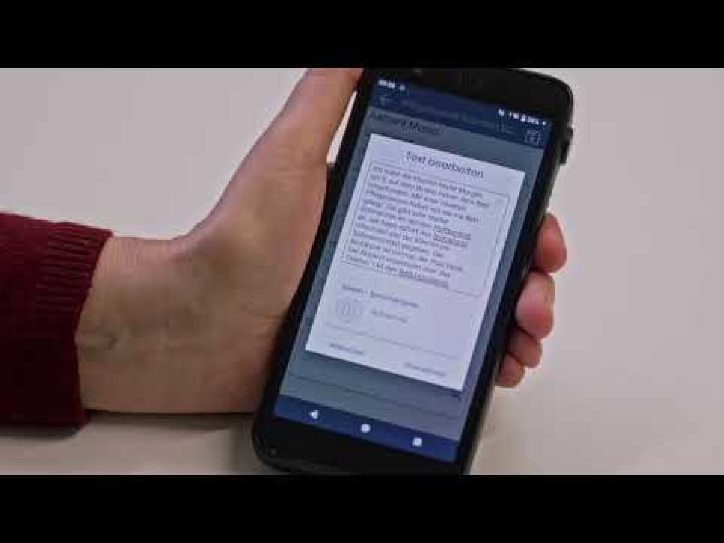 Eine Person, die ein Smartphone in der Hand hält, auf dessen Bildschirm eine Textnachricht angezeigt wird. Der Hintergrund ist einfarbig, und die Person trägt ein rotes Langarmshirt.