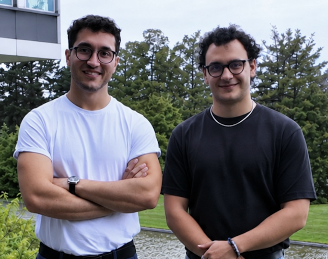 Deux jeunes hommes à lunettes, debout devant des arbres, à l'extérieur.